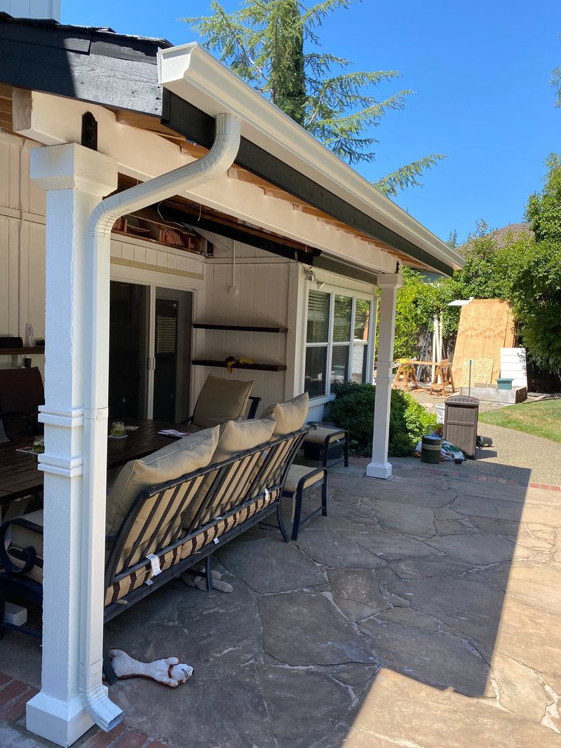 A patio with a couch and chairs under a porch with a white gutter.