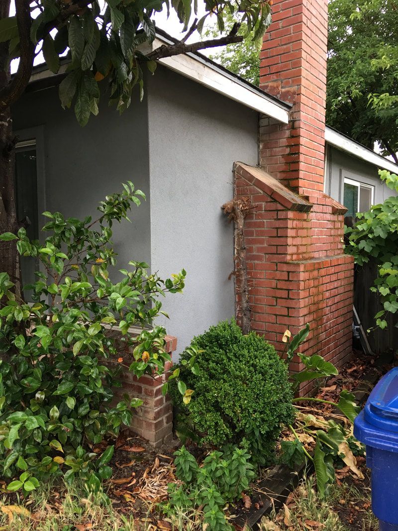 A brick chimney on the side of a house next to a blue trash can.