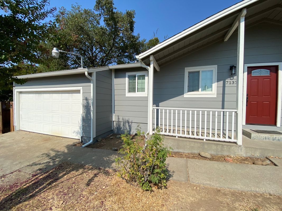 A gray house with a red door and a garage.