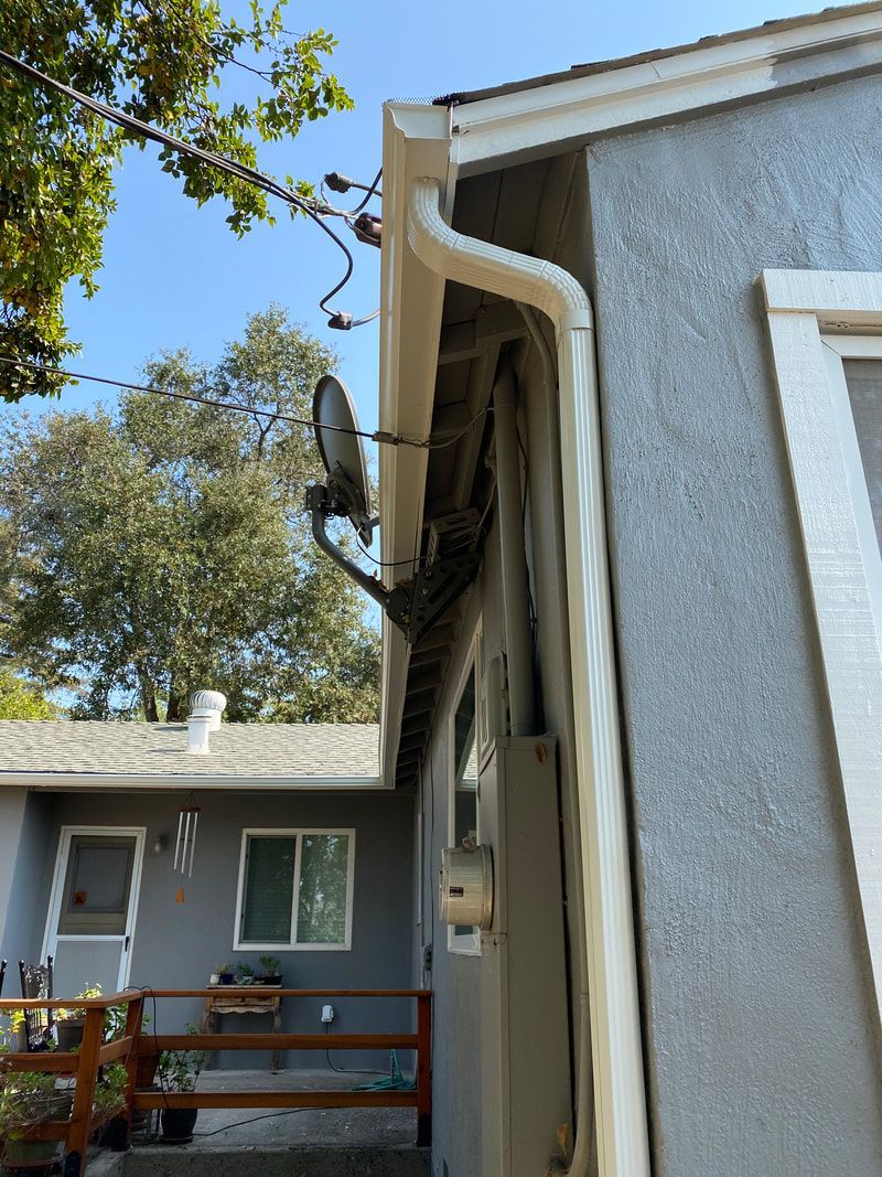 A house with a gutter on the side of it and a satellite dish on the roof.