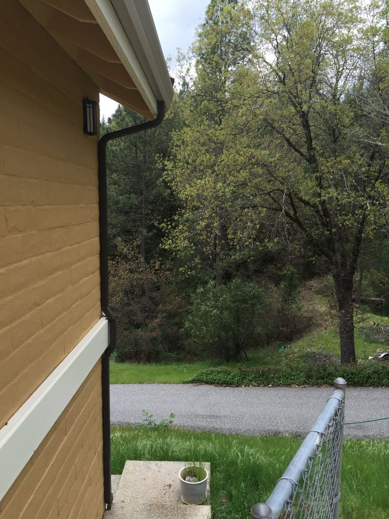 A brick house with a gutter on the side of it and a chain link fence.