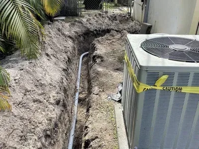 A large air conditioner is sitting in the dirt next to a hole in the ground.