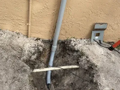 A pipe is being installed in a hole in the ground next to a wall.