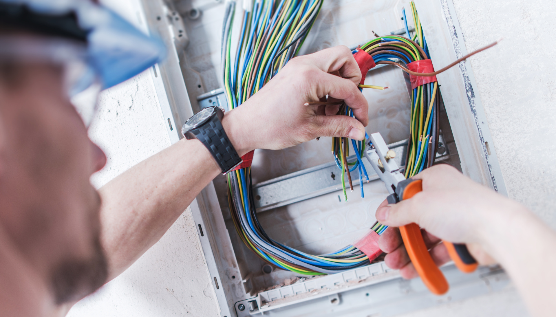 A man is working on an electrical box with a pair of pliers.