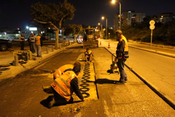 A group of construction workers work on a street at night to install wireless charging induction devices on the road.