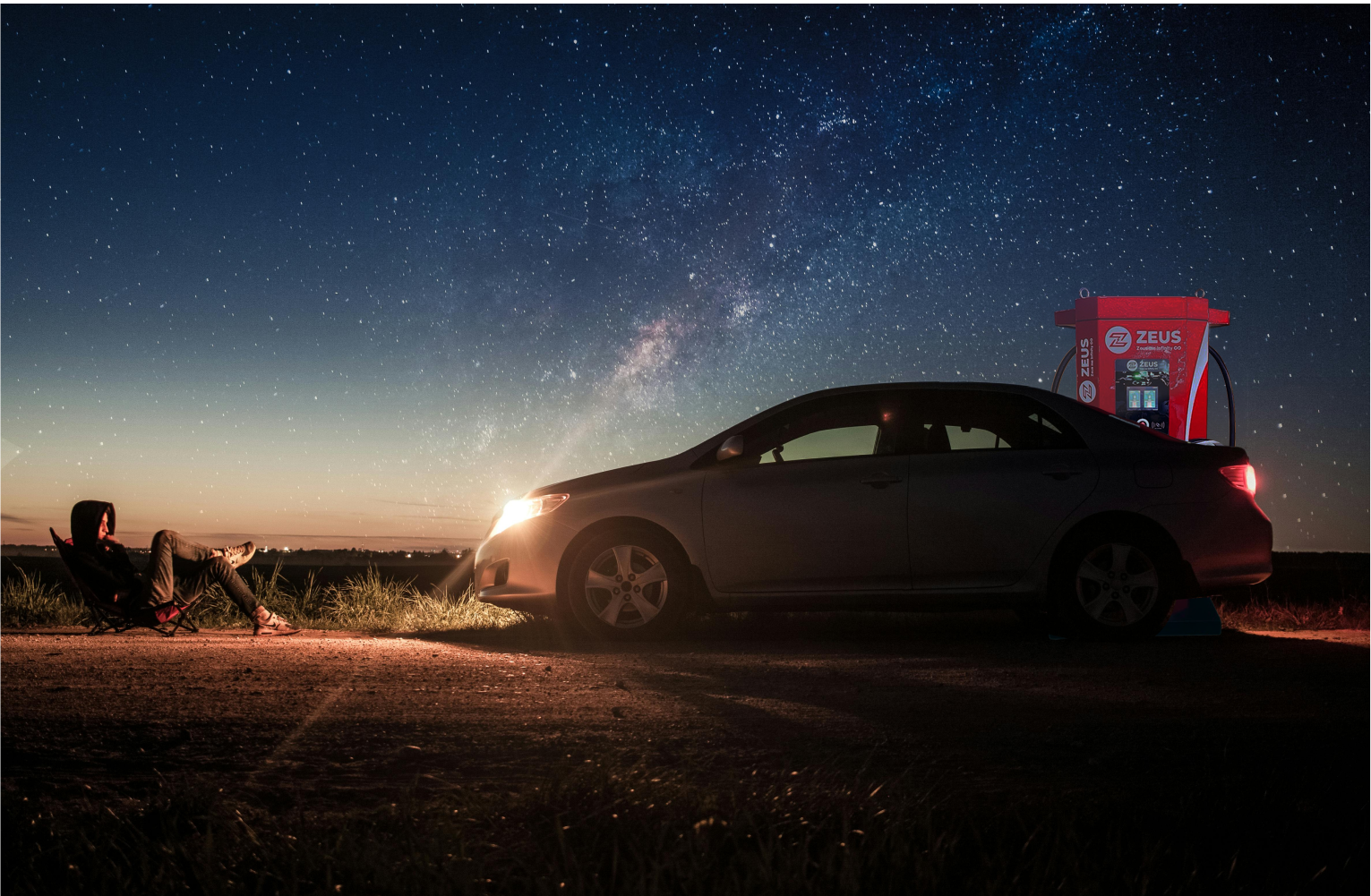 A car is parked outdoors next to a Zeus electric car charger.