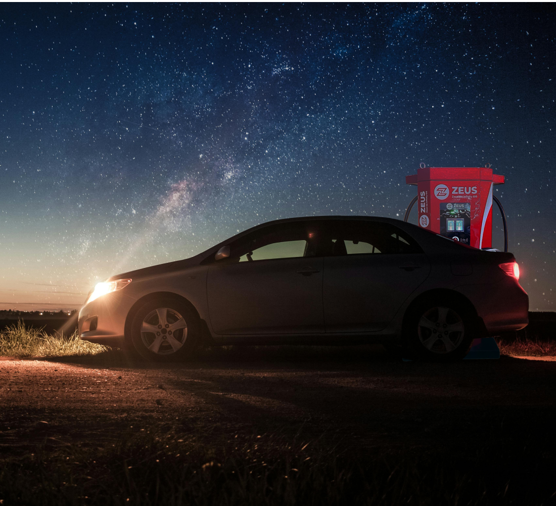 A car is parked outdoors next to a Zeus electric car charger.