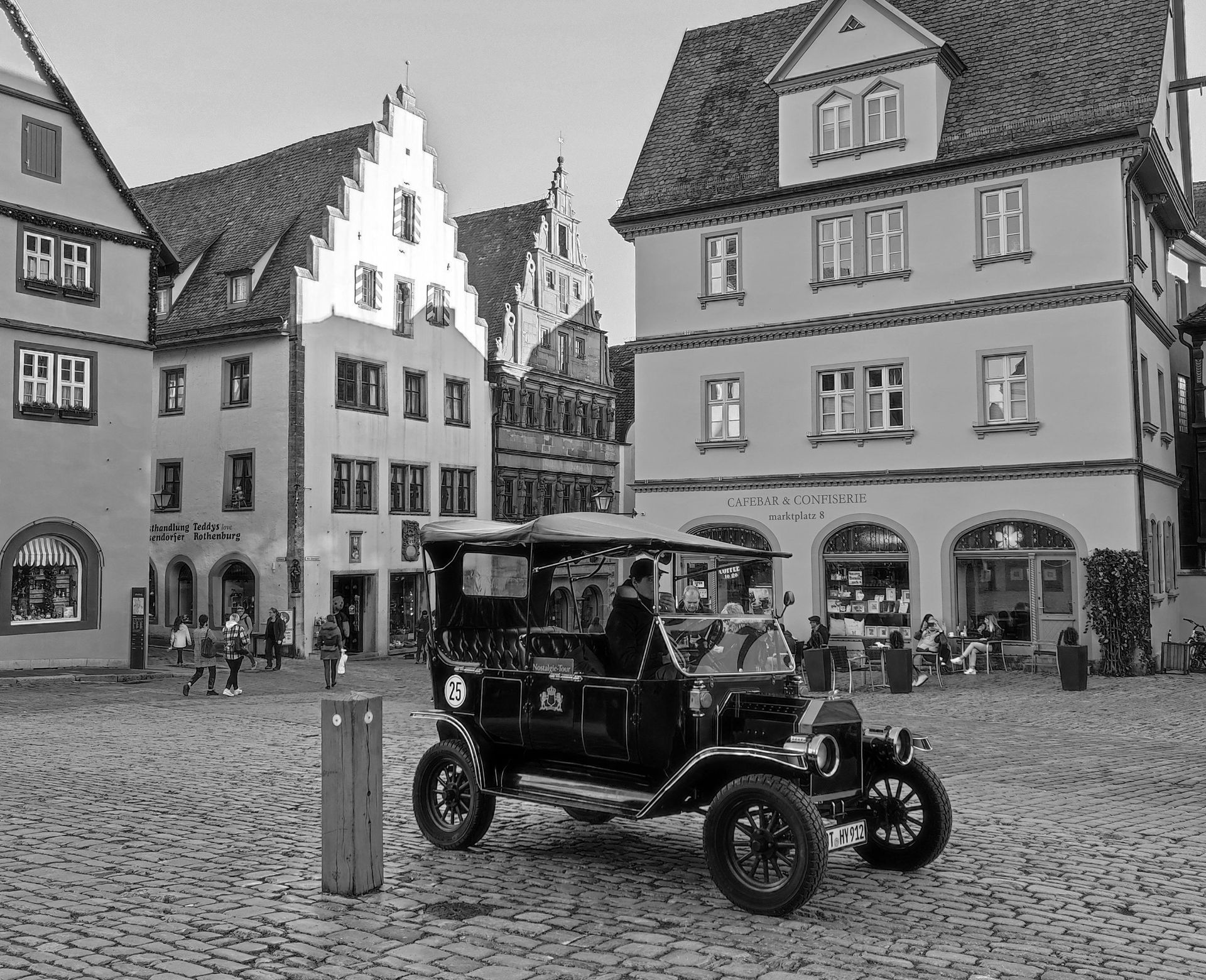 A black and white photo of an old car driving on a cobblestone street.