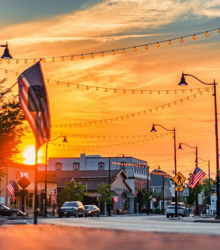 An american flag is hanging from a street light in front of a sunset