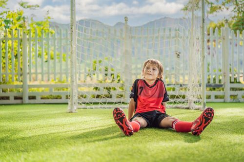a young football enthusiast resting on the fake grass installed by Gilbert Artificial Turf & Green