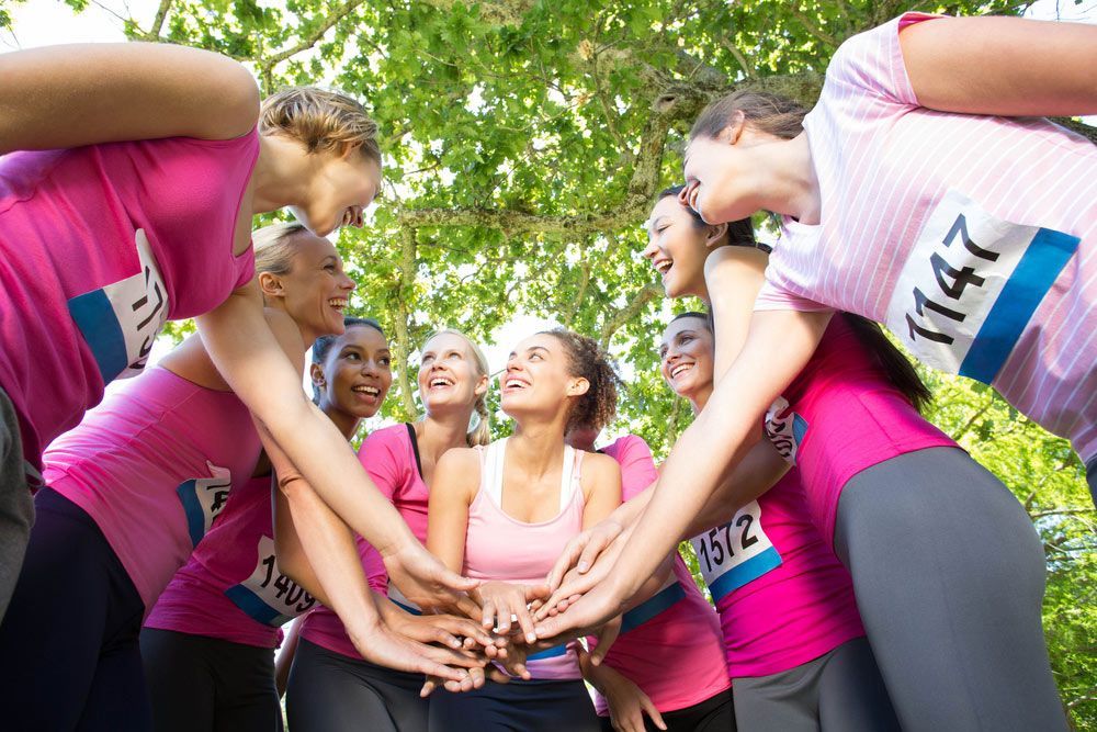 A Group Of Women Are Putting Their Hands Together In A Huddle — Pink Up Gold Coast in Southport, QLD