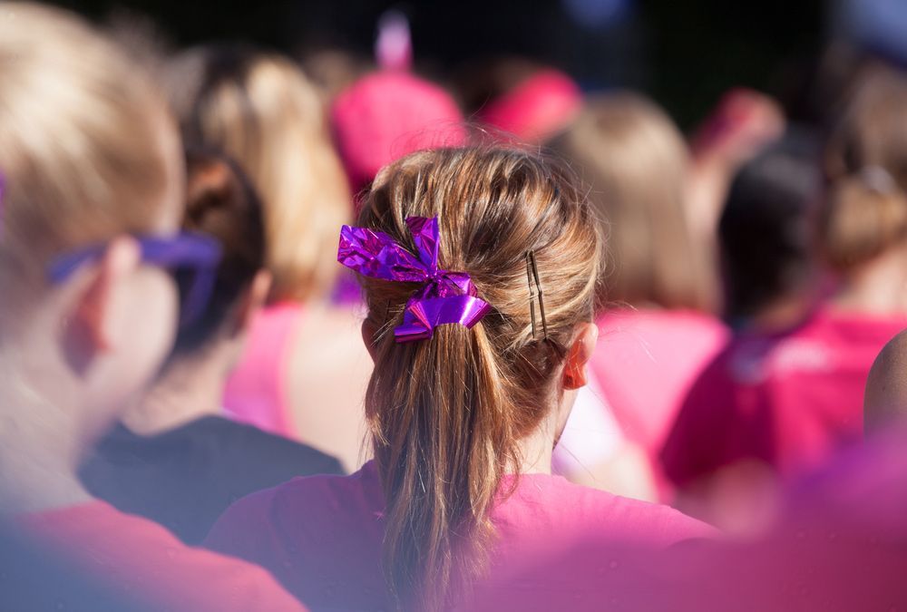 A Girl With A Purple Bow In Her Hair Is Sitting In A Crowd Of People — Pink Up Gold Coast in Southport, QLD