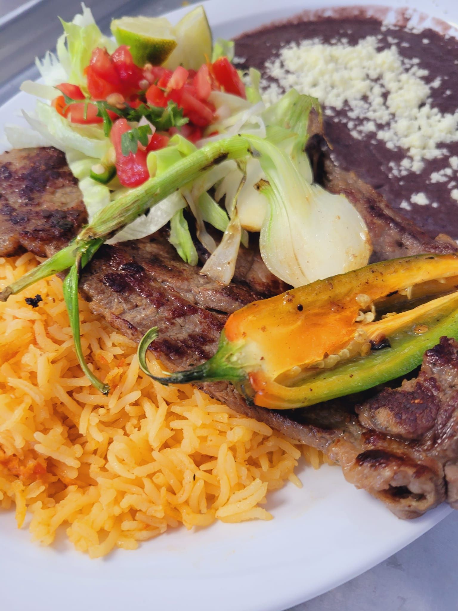 A white plate topped with rice , meat , beans and a salad.