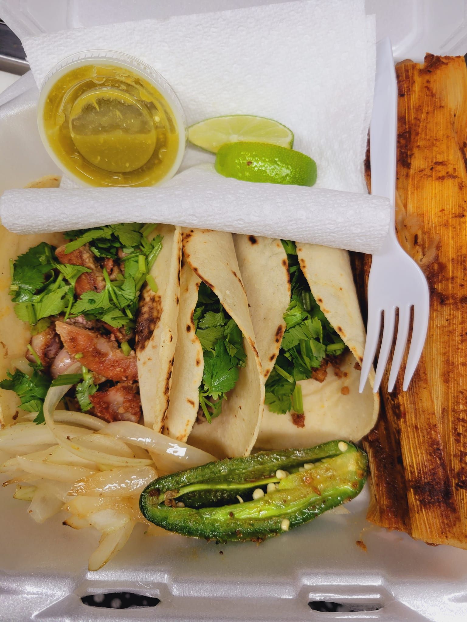A styrofoam container filled with tacos , onions , jalapenos and a fork.