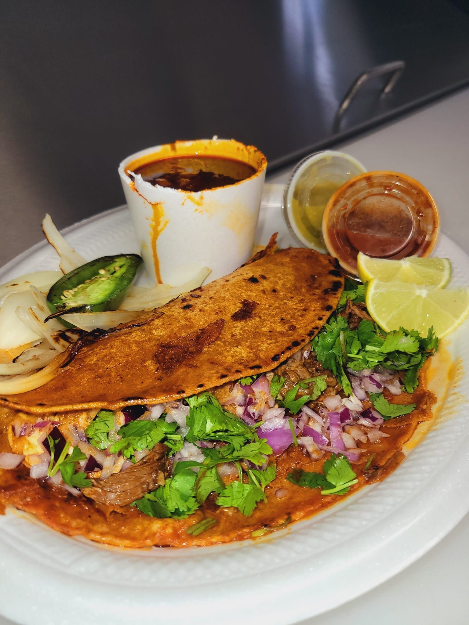 A white plate topped with a taco and a cup of soup.