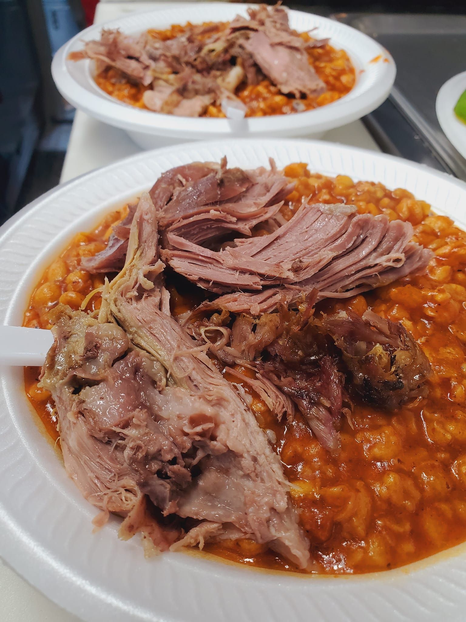 Two bowls of food with meat and beans on a table.