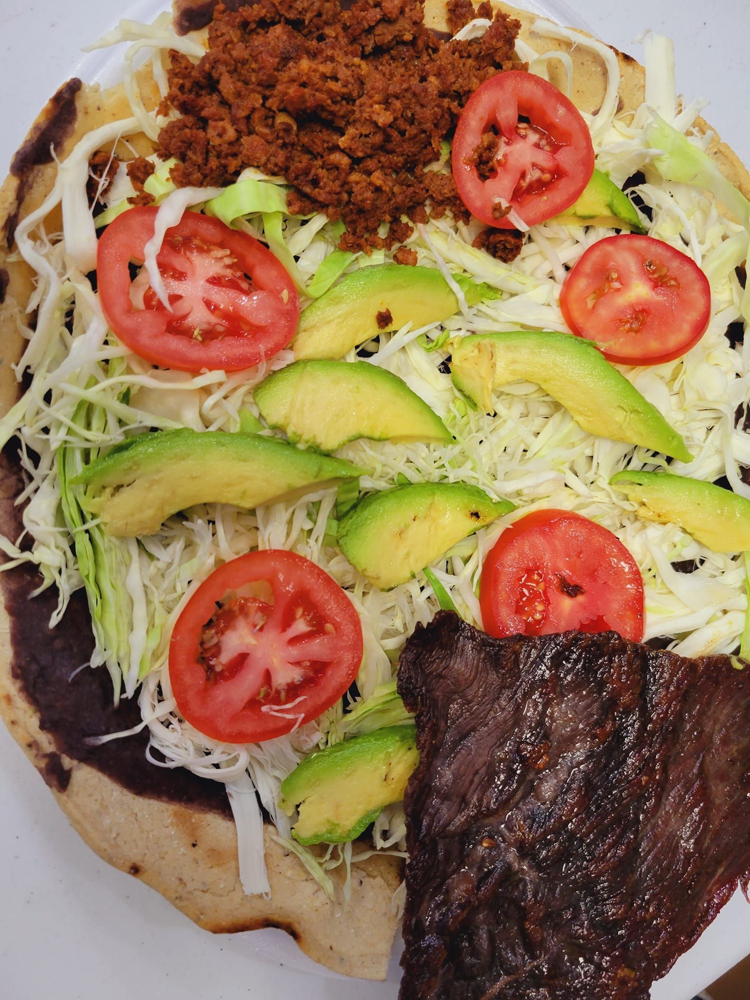 A pizza with tomatoes , cabbage , avocado and meat on it.