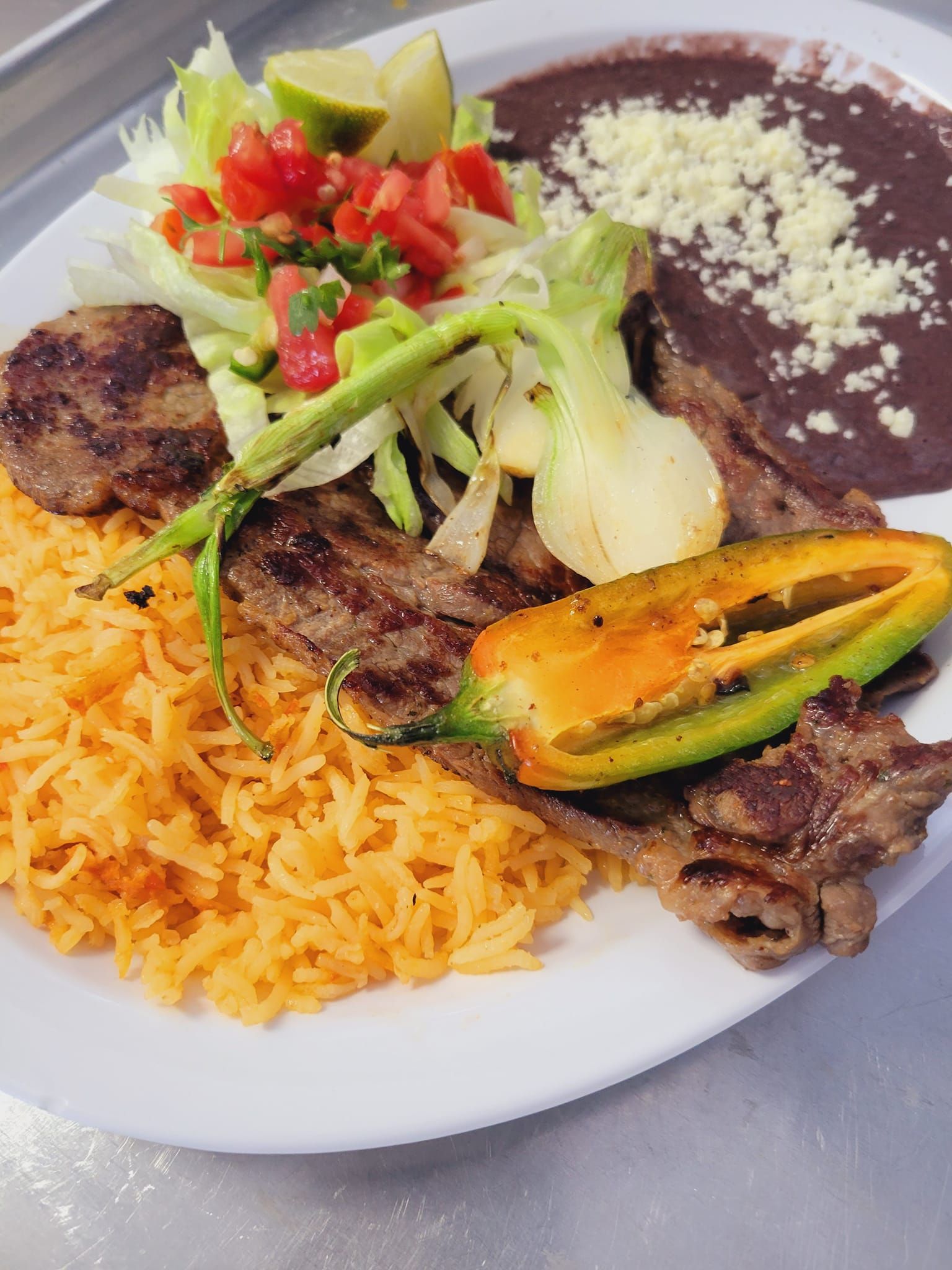 A white plate topped with rice , meat , beans and vegetables.