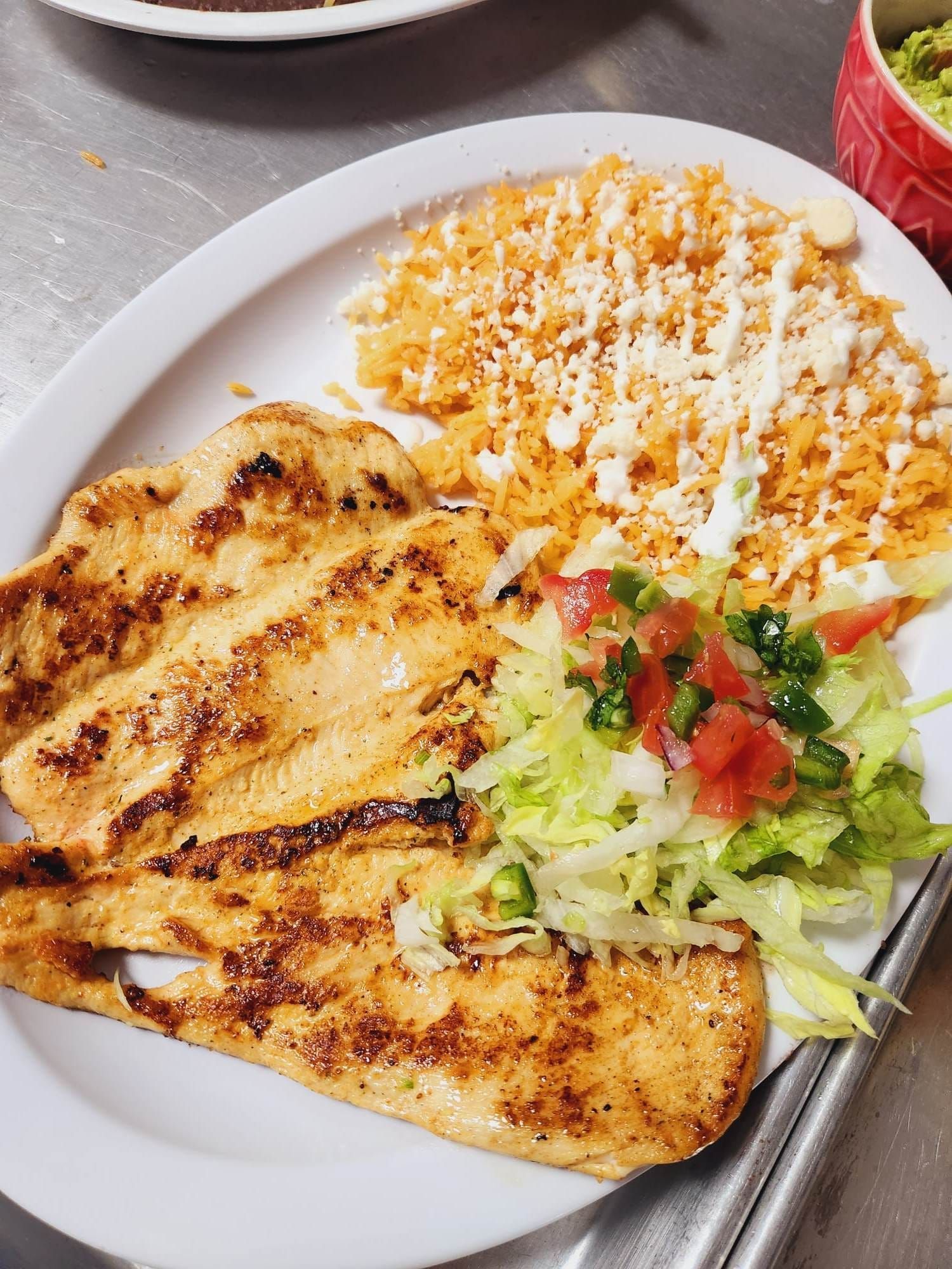 A white plate topped with grilled chicken , rice and salad.