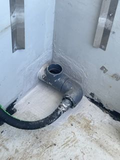 A hose is connected to a pipe in a corner of a room.