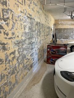 A white car is parked in a garage next to a brick wall.