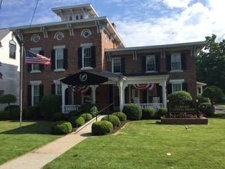 Brick building with porch, American flag, and manicured lawn. Entrance has black awning.