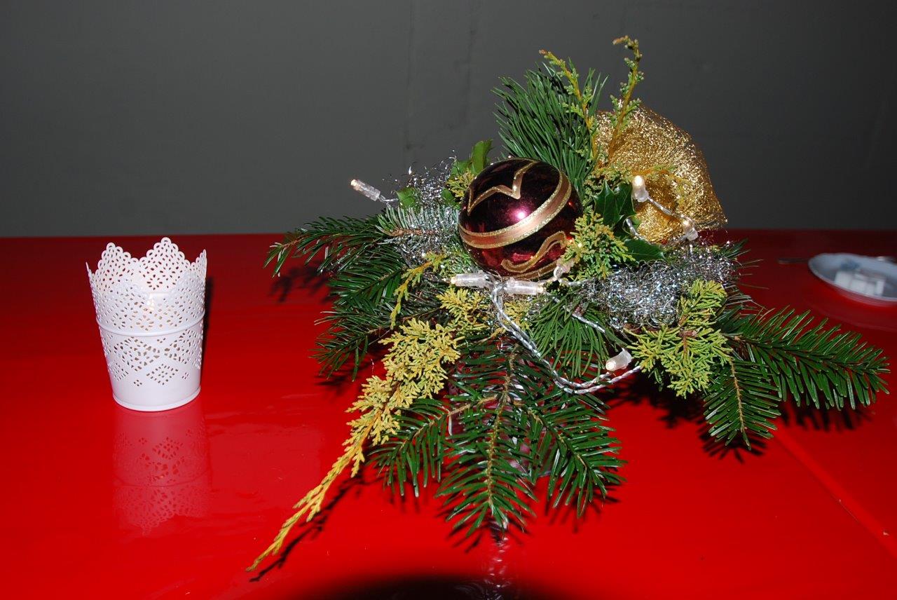 Eine Weihnachtsdekoration auf einem roten Tisch neben einem weißen Kerzenständer.