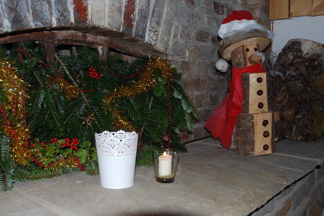 Auf einem Tisch steht eine Kerze neben einem hölzernen Schneemann mit Weihnachtsmannmütze.