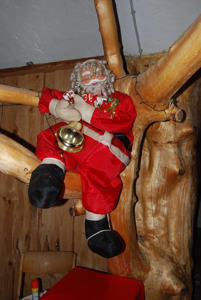 Eine Weihnachtsmannpuppe sitzt auf einem Ast und hält eine Glocke.