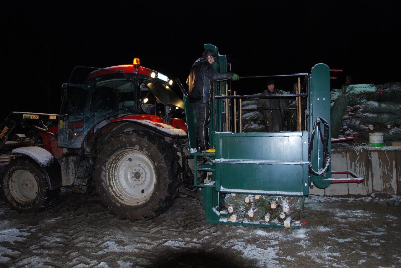 Ein Mann steht nachts neben einem Traktor im Schnee.