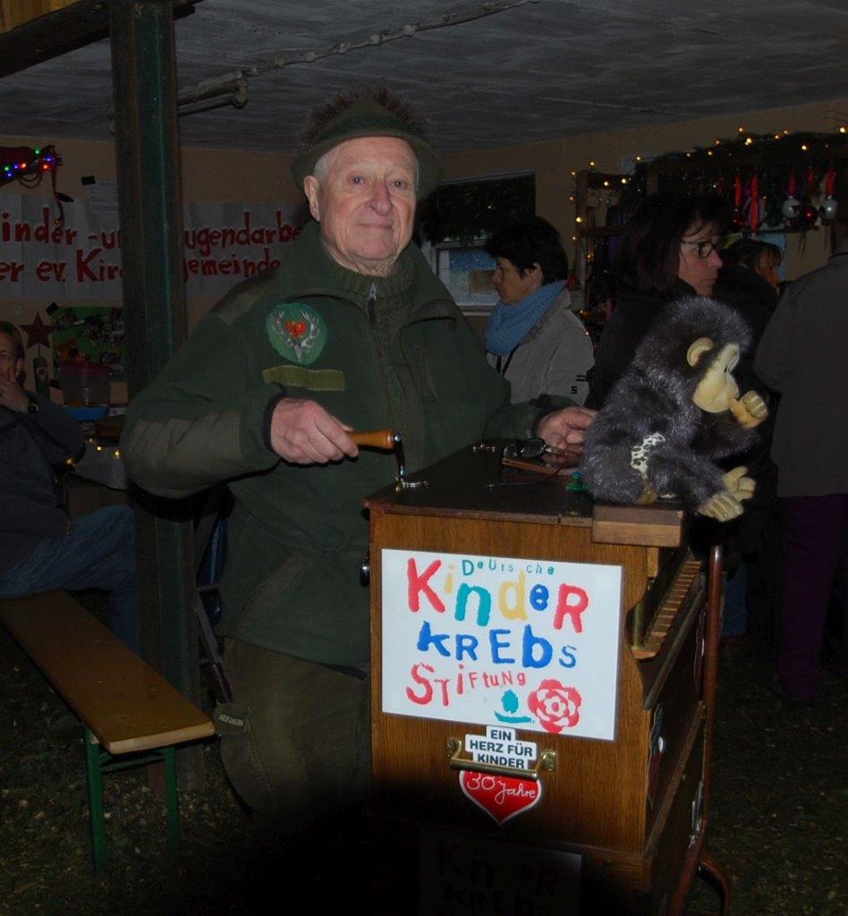 Ein Mann hält einen ausgestopften Affen vor einem Schild mit der Aufschrift „Kinder Krebs“