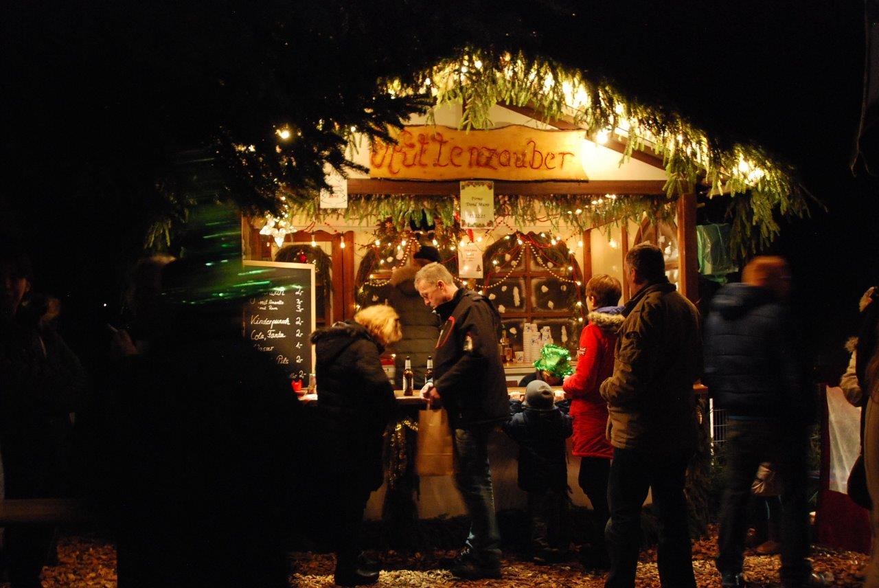 Eine Gruppe von Menschen steht vor einem Stand auf einem Weihnachtsmarkt.
