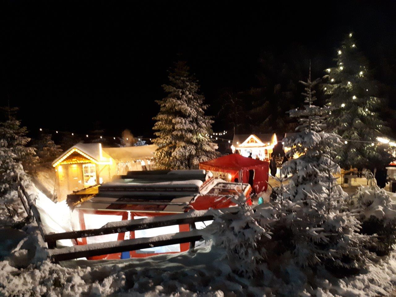 Aufnahme von den Ständen auf dem Weihnachtsmarkt umgeben von schneebedeckten Tannen