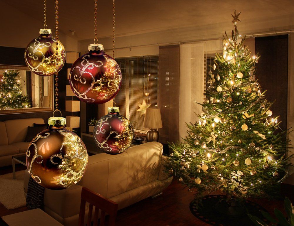 Weihnachtsbaumkugeln hängen in einem weihnachtlichen Wohnzimmer. Der geschmückte Weihnachtsbaum ist im Hintergrund