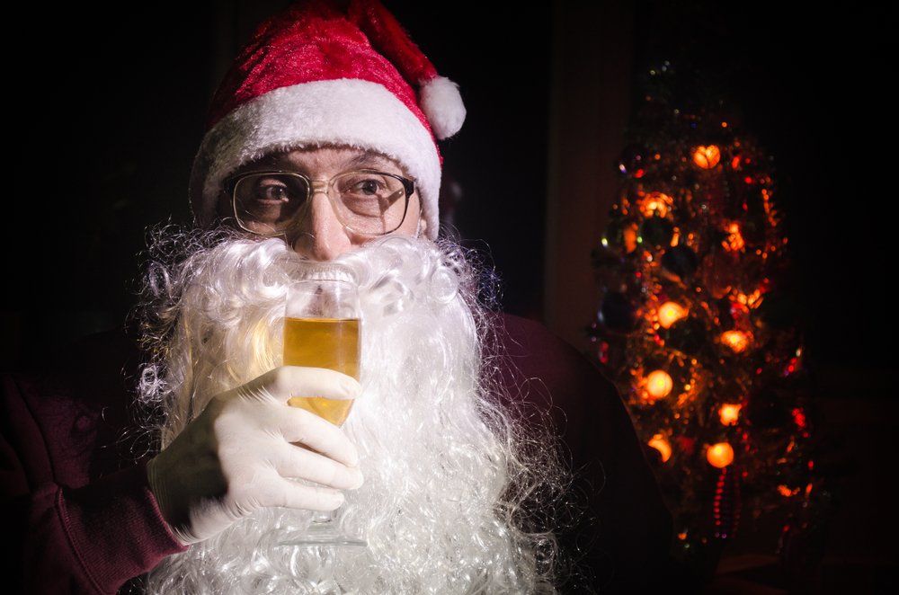 Nahaufnahme von einem Weihnachtsmann der Bier trinkt. Weihnachtsbaum im Hintergrund
