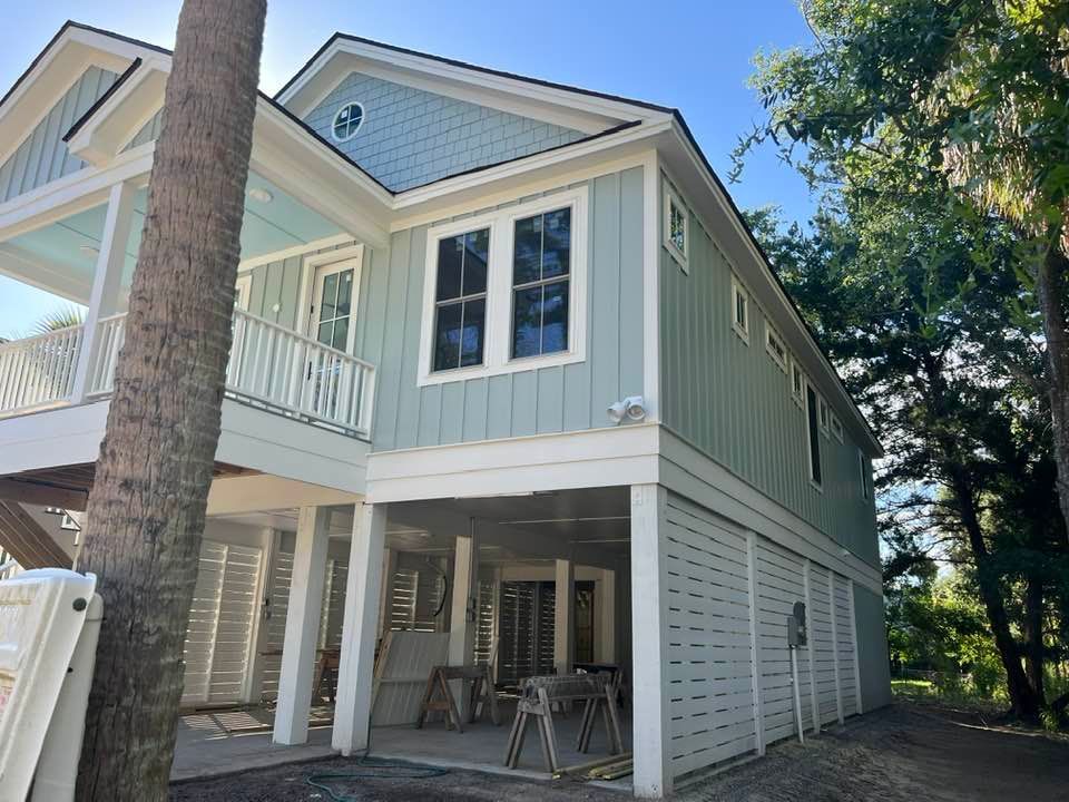 Two-story light blue house with white trim, balcony, and shaded ground-level patio under a clear sky