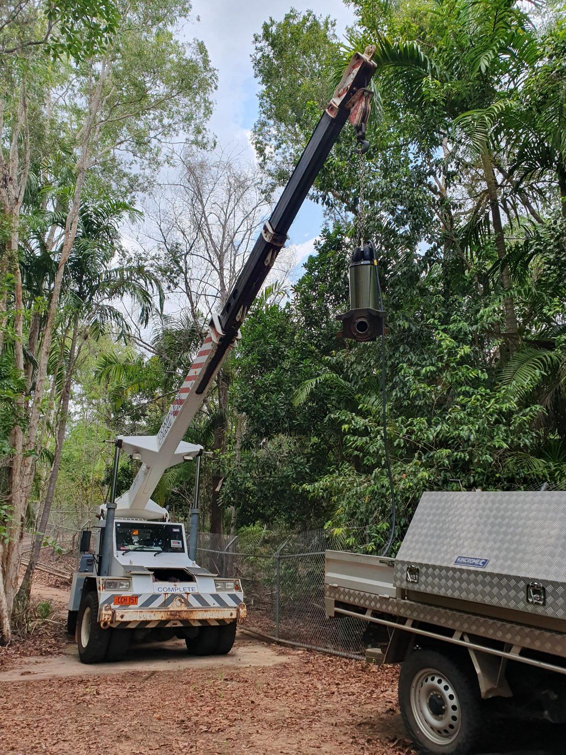 A truck with a crane attached to it is parked next to a tree.
