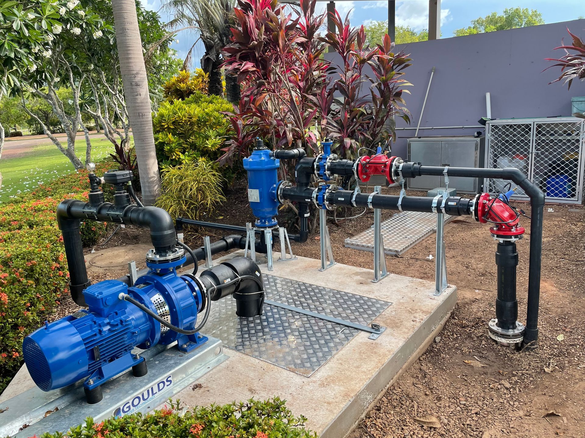 A blue pump is sitting on top of a concrete platform next to a bunch of pipes.