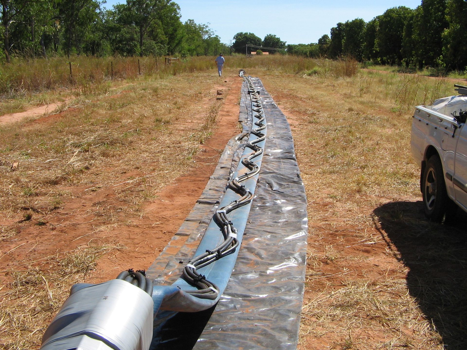 A white truck is parked in a field next to a blue pipe