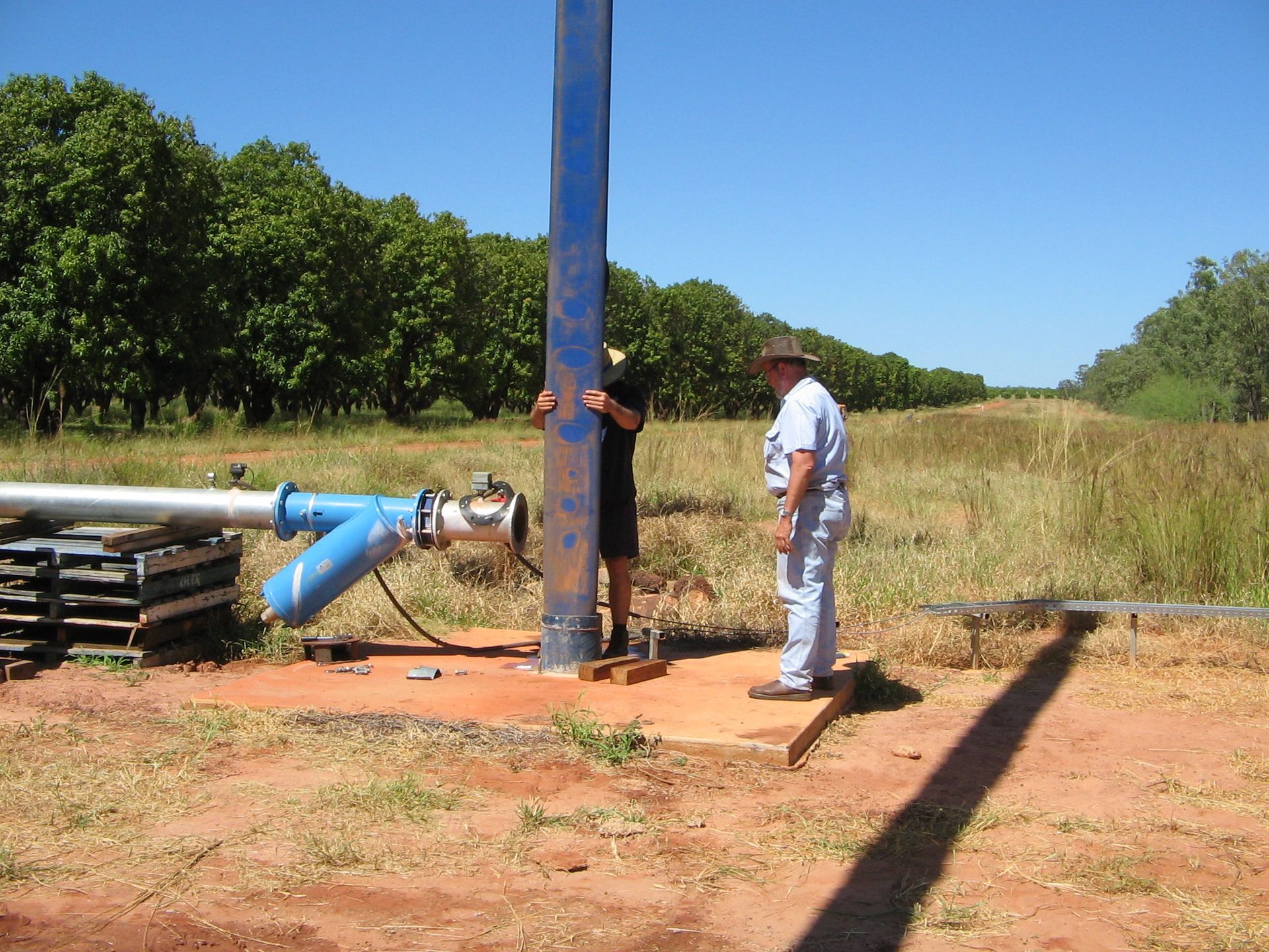Two men standing next to a blue pipe in a field