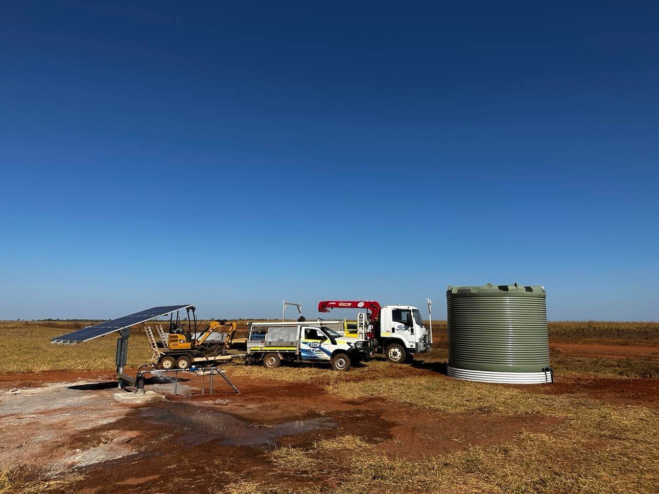A truck is parked in a field next to a water tank.