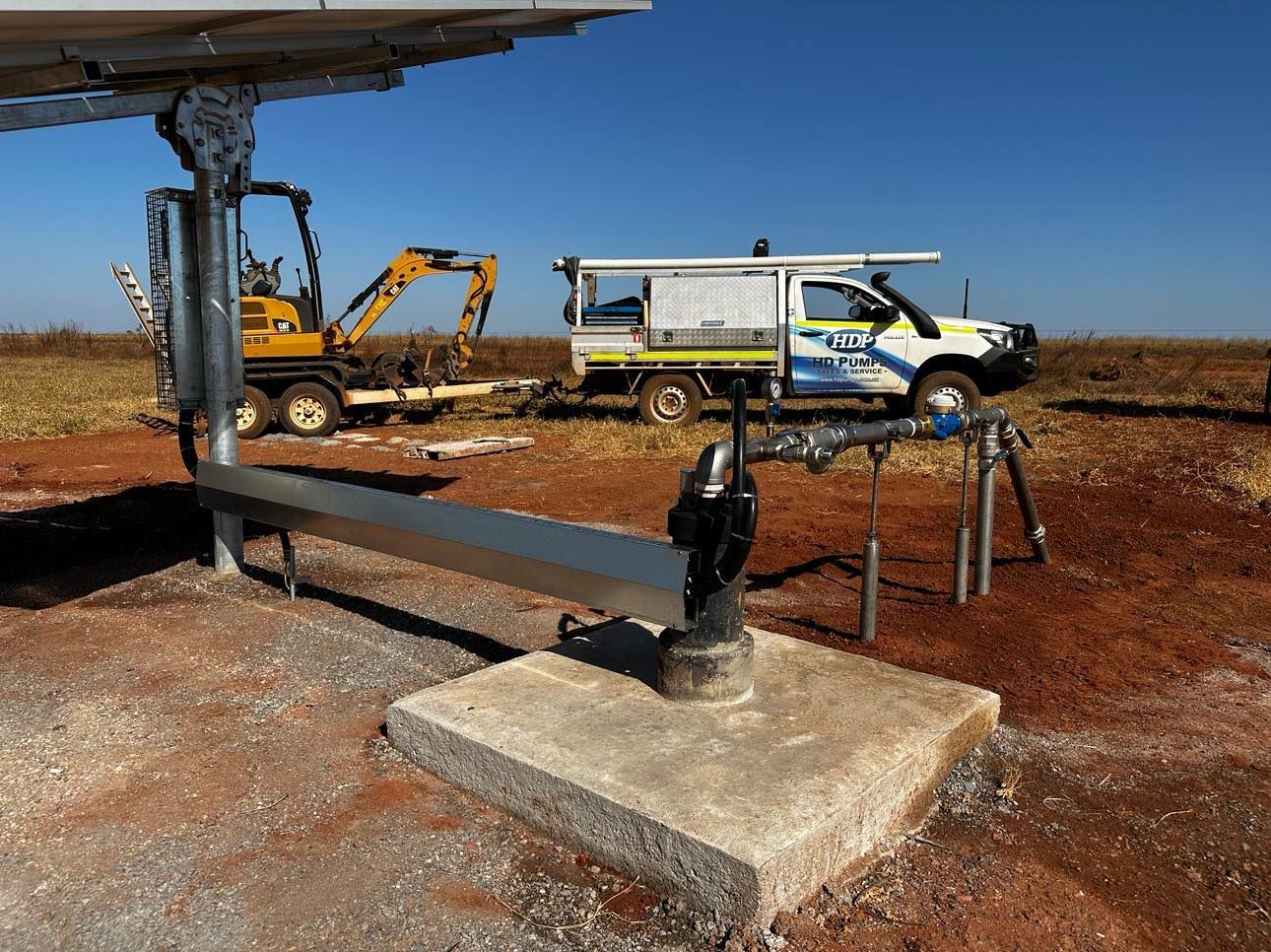 A white van is parked in a dirt field next to a yellow excavator.