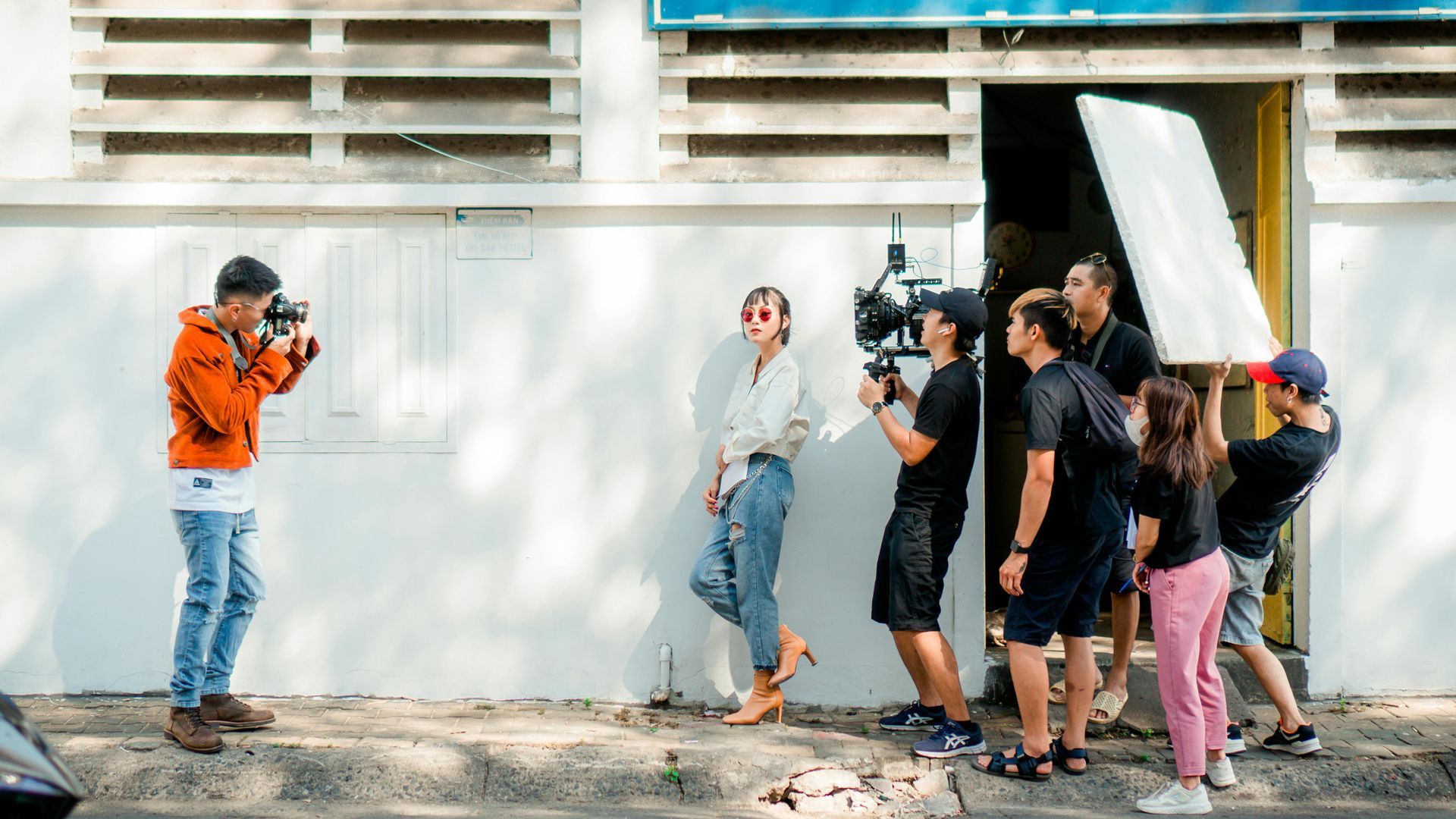 A group of people with a video camera are filming in front of a white building.