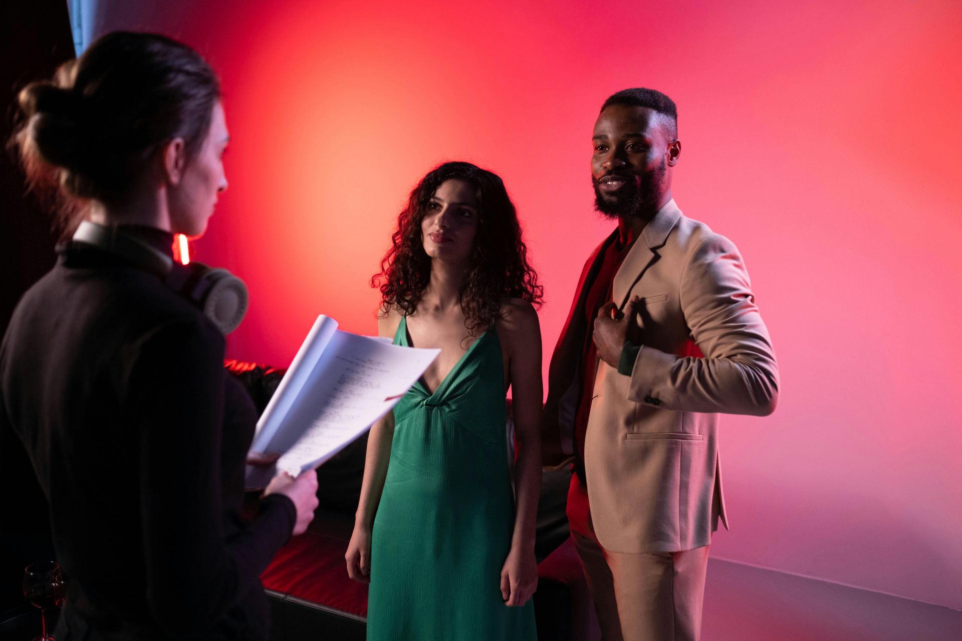 A man and a woman being briefed by another woman, standing next to each other in front of a red background.