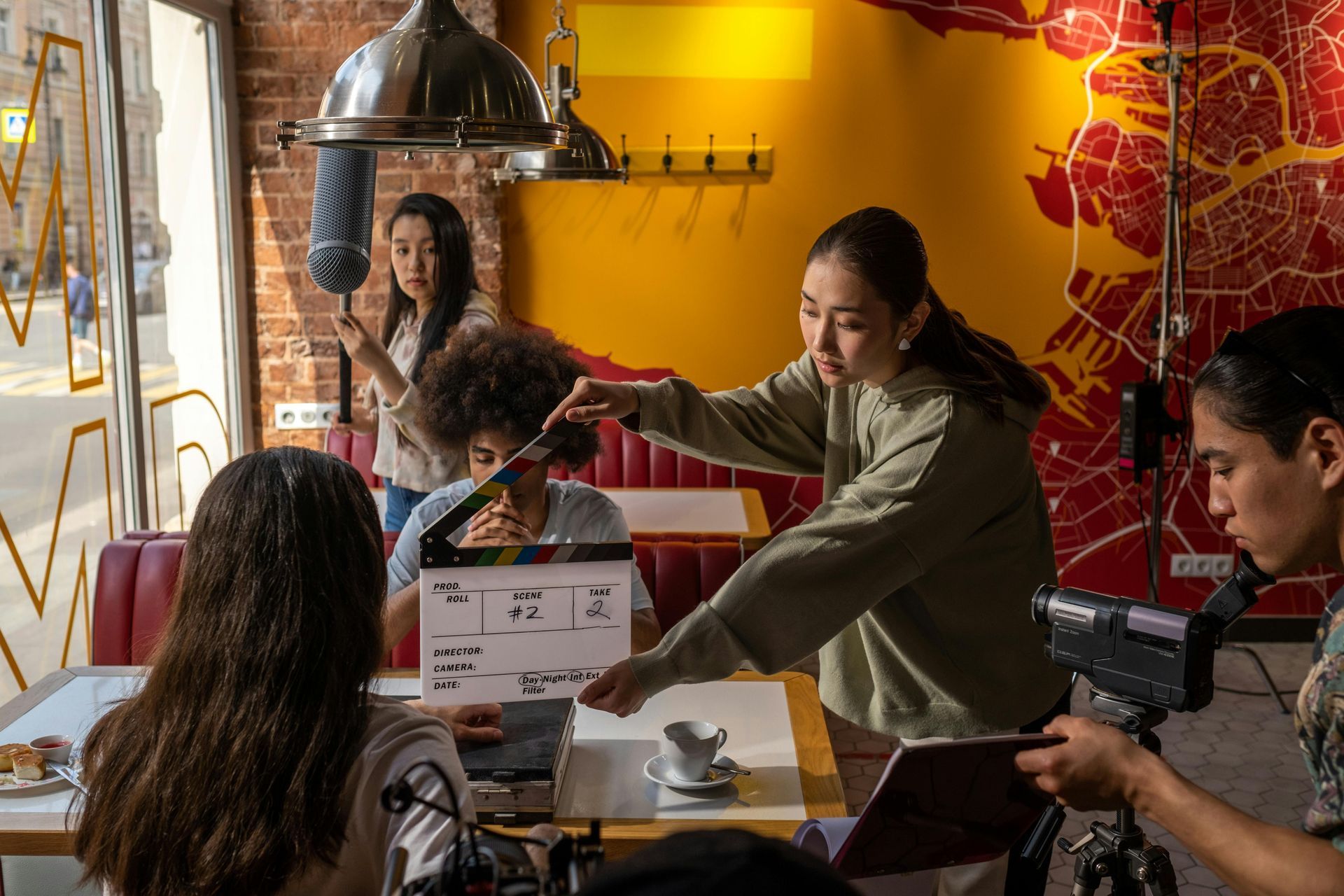 A group of people are sitting at a table in a restaurant while being filmed