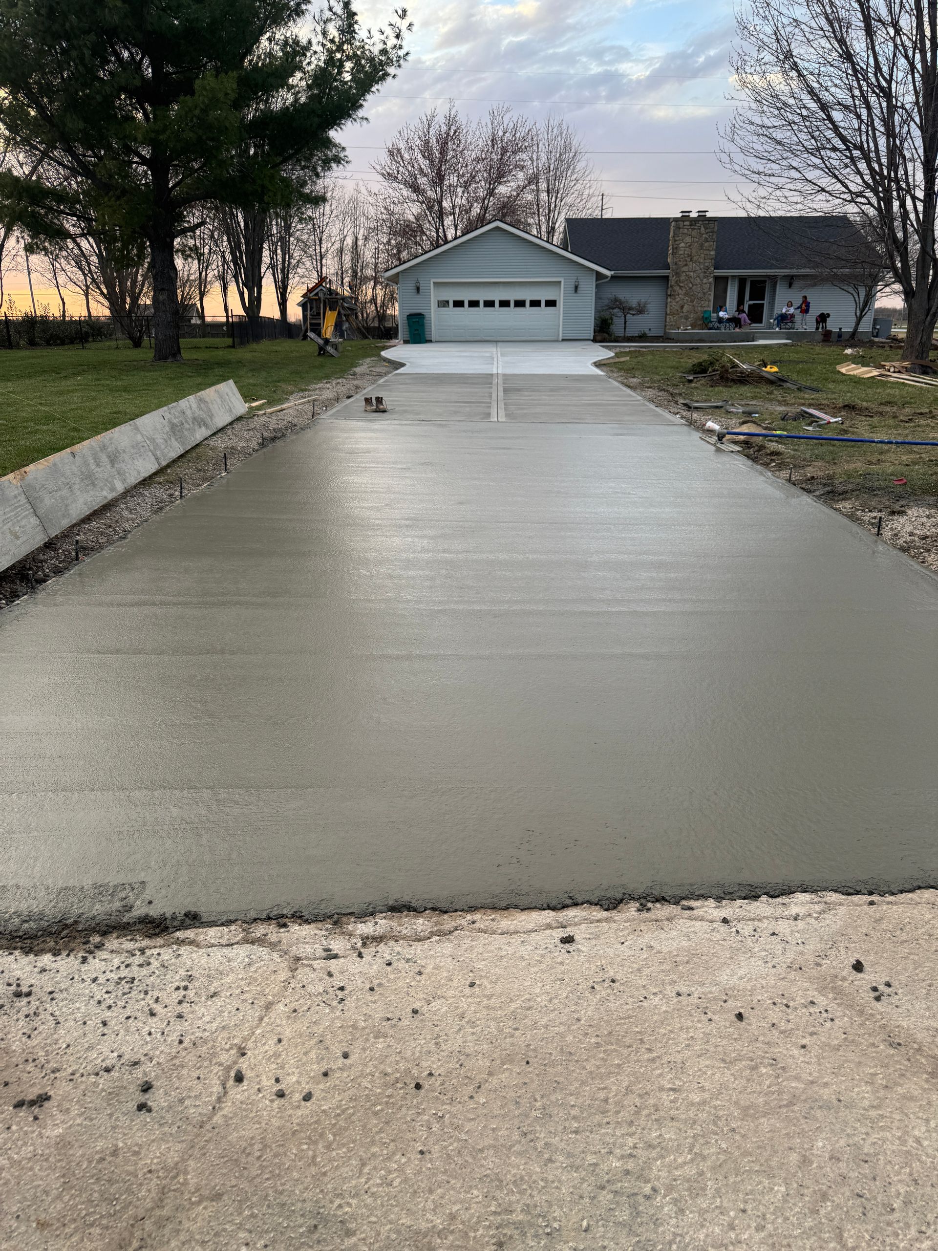 Freshly poured concrete driveway leading to a house with an attached garage under a soft, overcast sky.