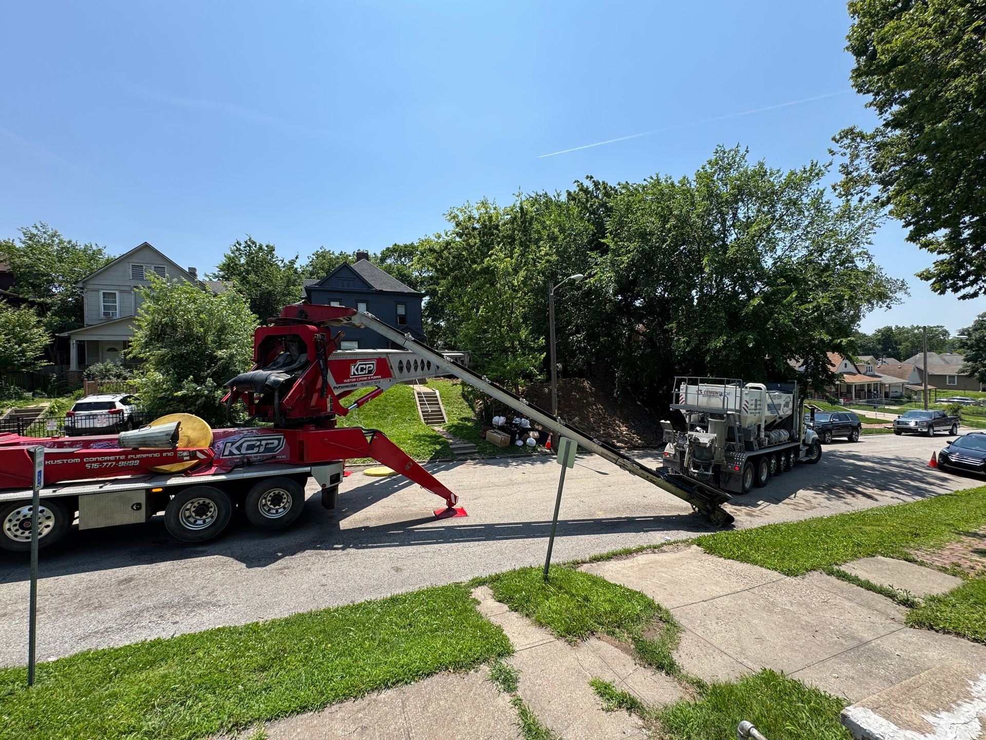 Truck-mounted conveyor extending over a residential area, with a worker near a tree.