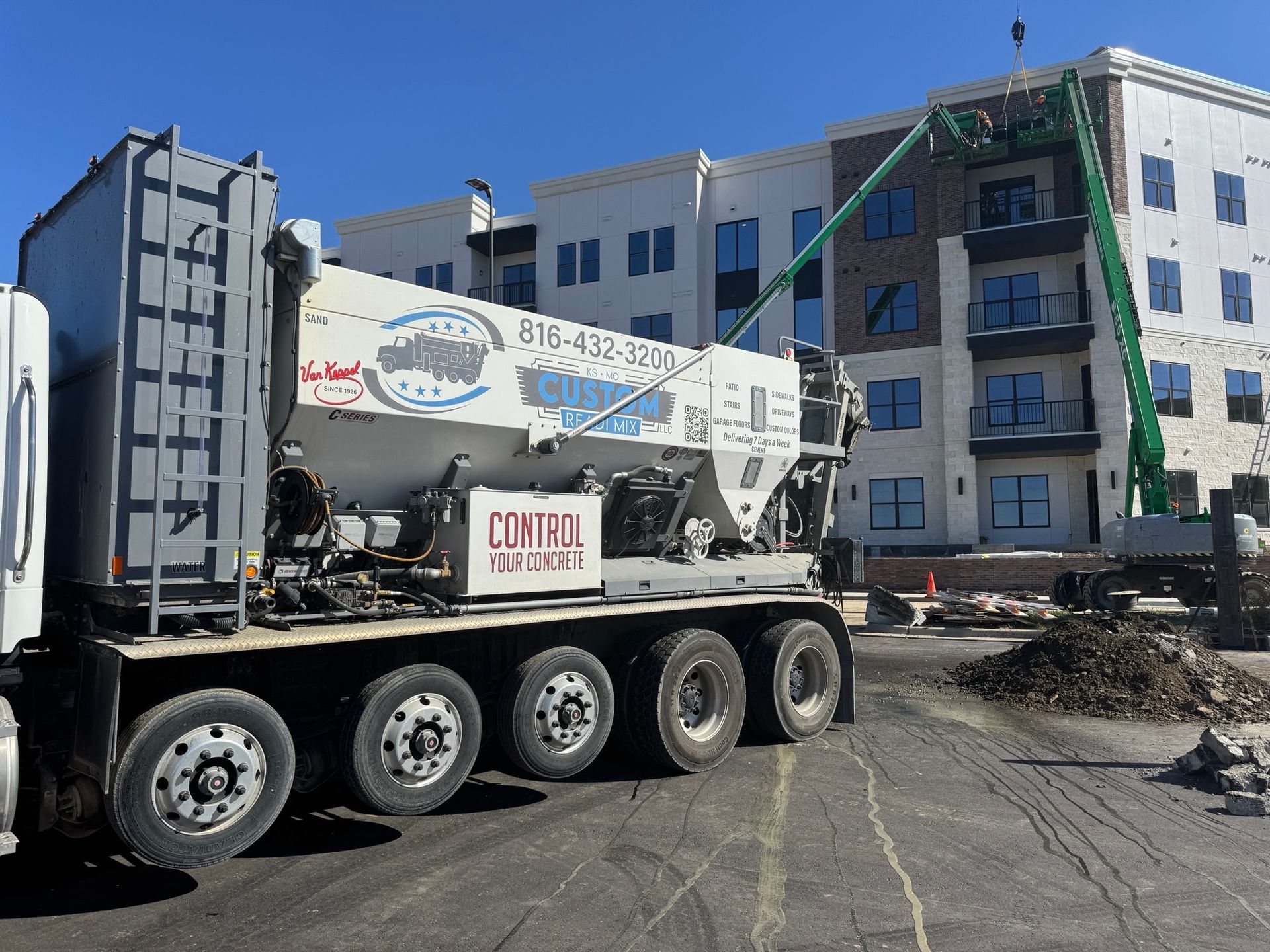 A volumetric concrete mixer truck parked in front of a multi-story apartment building under construction.