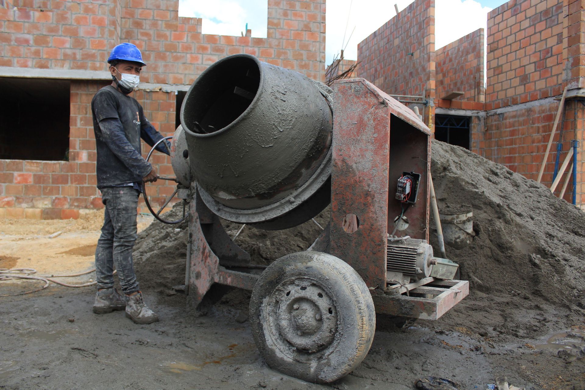 Worker beside cement mixer on a construction site with brick walls and piles of sand