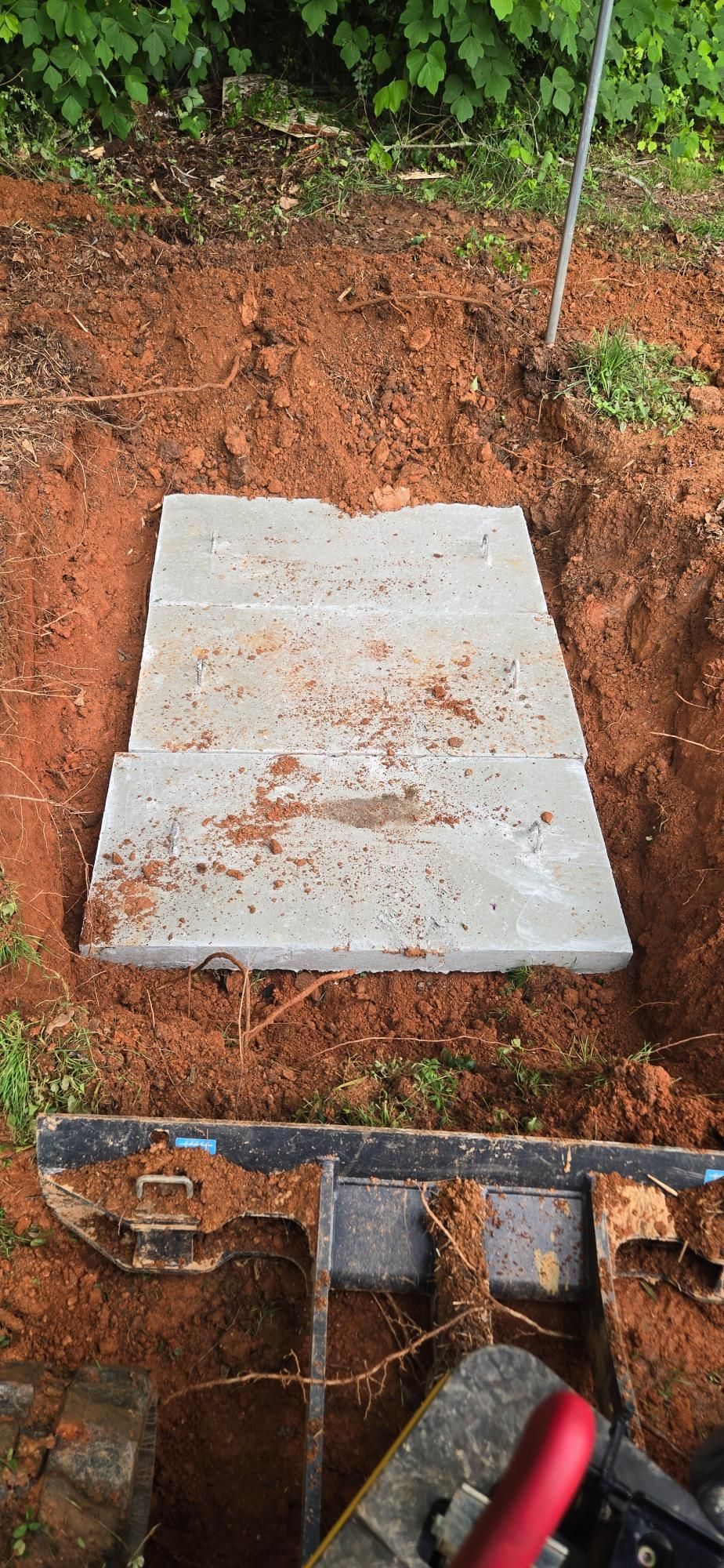 A rectangular concrete slab sits in a dirt excavation. Shovel equipment is visible at the bottom of the frame.